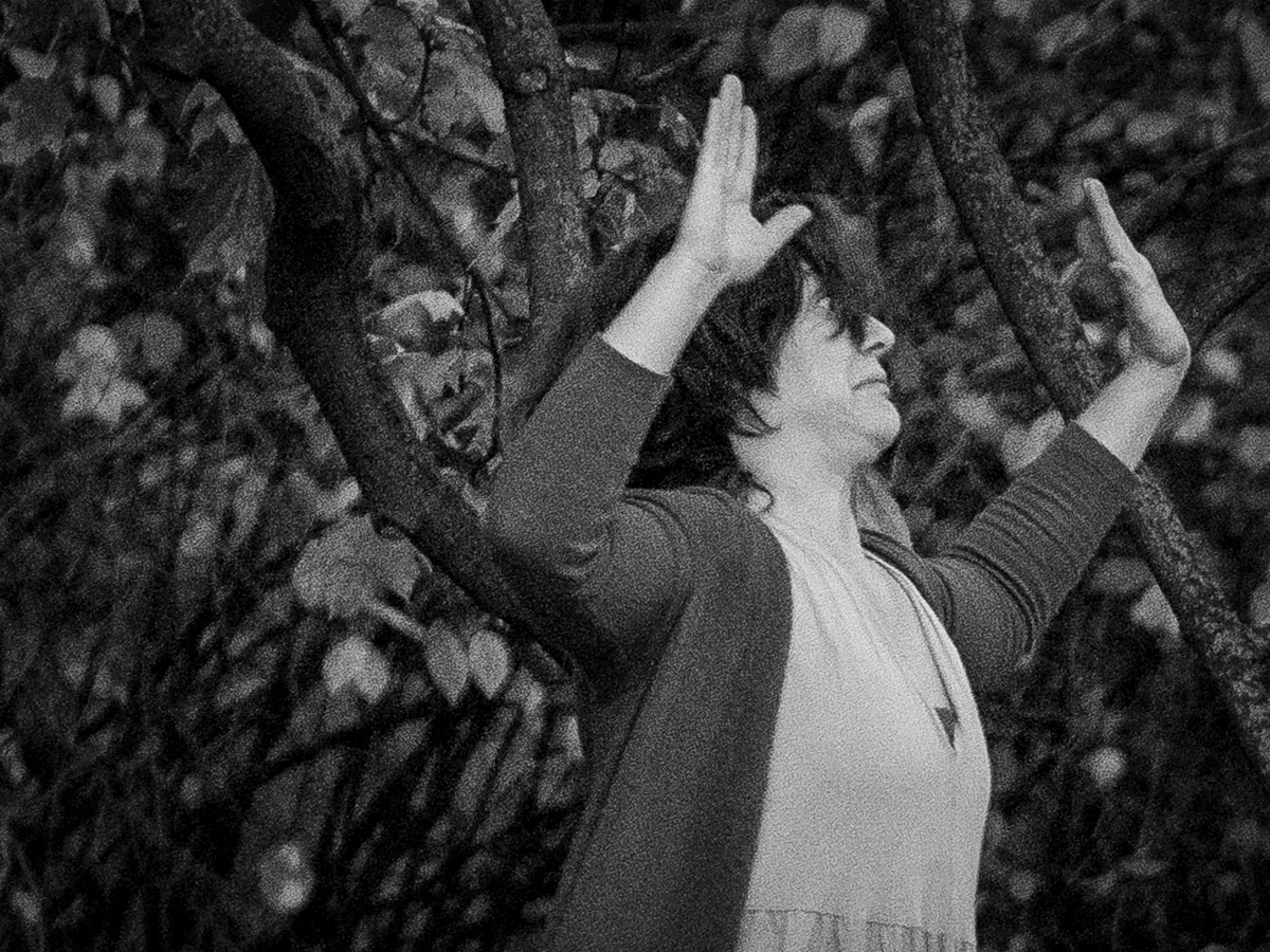 Woman raising both hands among dark tree branches